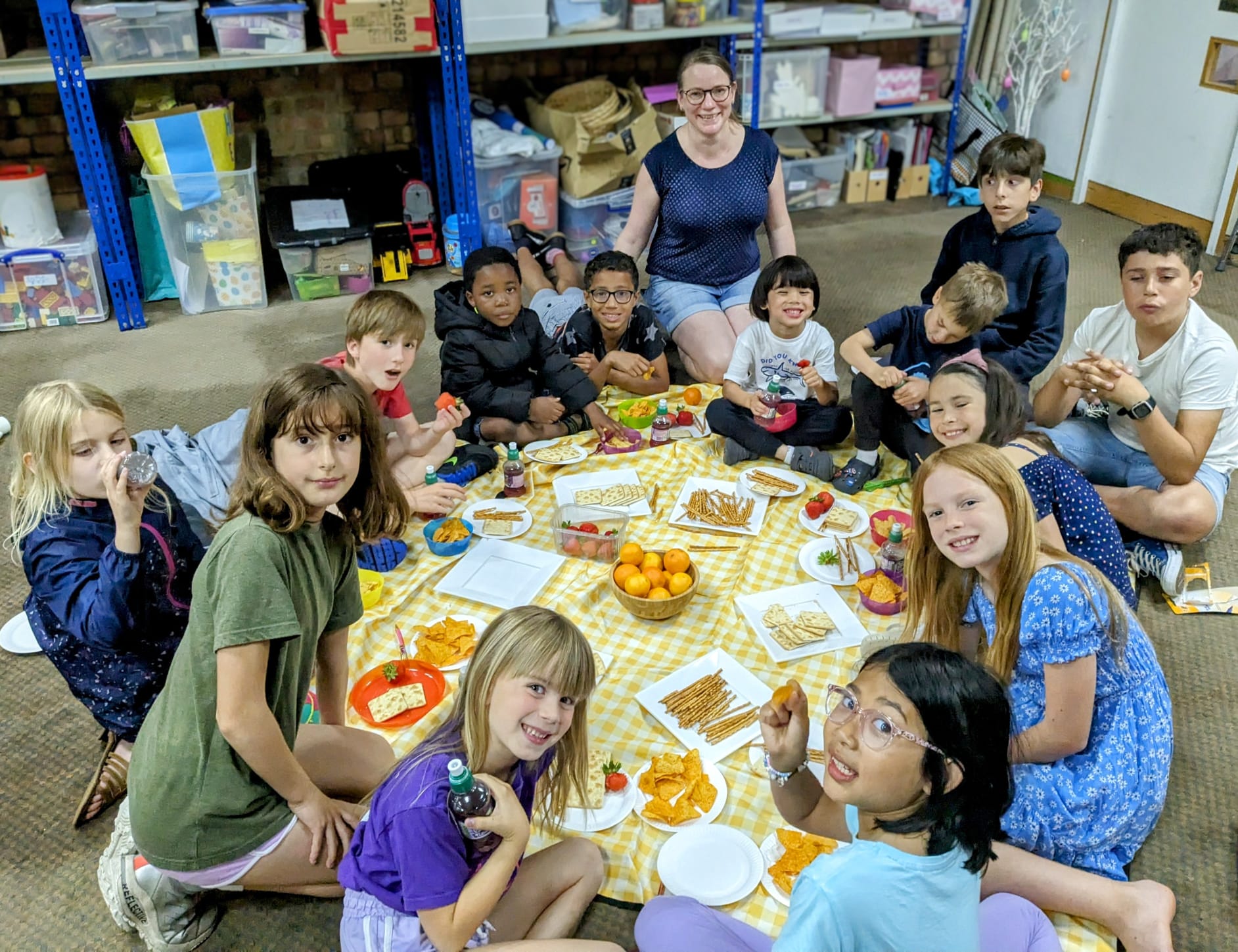 Group of children having a picnic with a wall of toys in the background